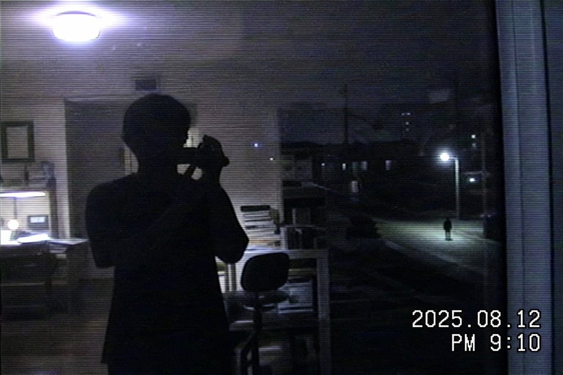 夜の窓ガラス。映り込みの奥、街灯の下に人がひとり立っている
